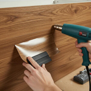 A person applying wood paneling with a heat gun, focusing on the surface for a smooth finish.